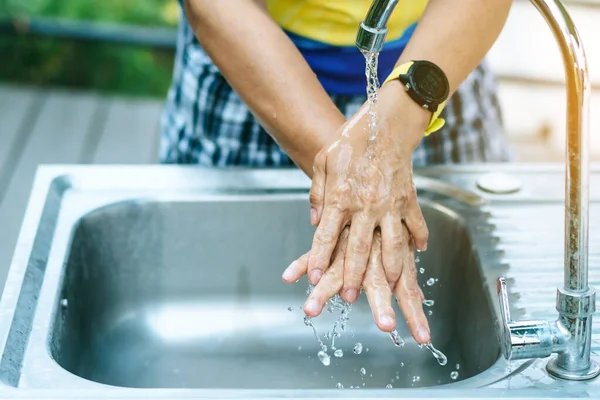 A woman washing hands from the tap with pink soap in a aluminium tub. Concepts of Flu virus, Covid-19 (Coronavirus disease). Selective focus.