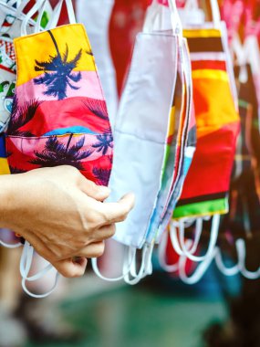 Sokak pazarında satılan mikropları (Covid-19) önlemek için moda kumaş pamuğundan yapılan el yapımı renkli maske çeşitliliğine yakın. Arkaplanda bulanıklık olan seçici odak.