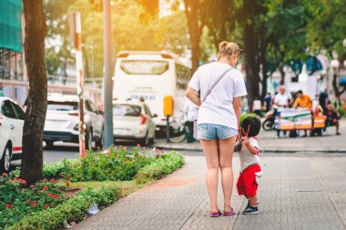 Güneşli bir yaz gününde, küçük oğluyla birlikte kaldırımda yürüdüğü arka manzara.