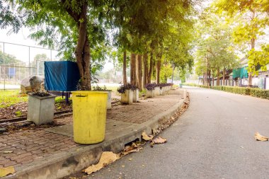 Çevreyi korumak için yürüyüş yolunun yanındaki parkta eski sarı bir çöp tenekesi..
