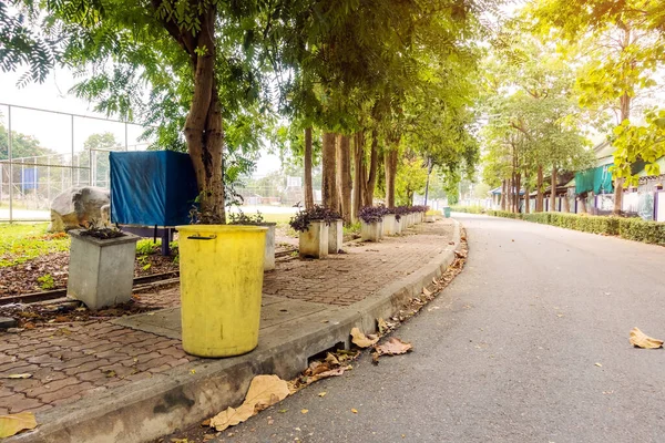 Çevreyi korumak için yürüyüş yolunun yanındaki parkta eski sarı bir çöp tenekesi..