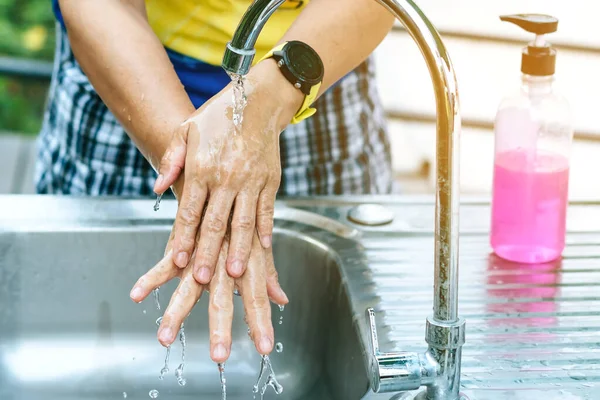 A woman washing hands from the tap with pink soap in a aluminium tub. Concepts of Flu virus, Covid-19 (Coronavirus disease). Selective focus.