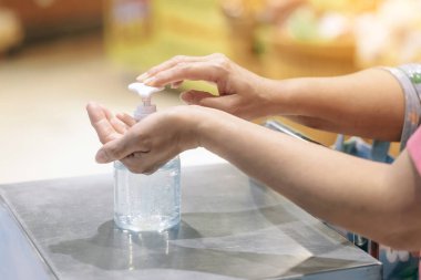 Kadın süpermarkete girmeden önce Corona virüsünün (Covid-19) yayılmasını önlemek için ellerini temiz alkol jeli şişesiyle yıkar. Covid-19 salgını sırasında alışveriş.