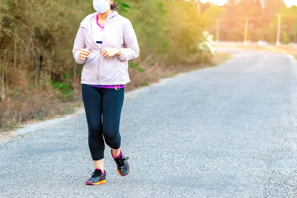 Sportive woman wears protective mask on face jogging for good health on road beside irrigation canal due to the corona virus (Covid-19) outbreak.