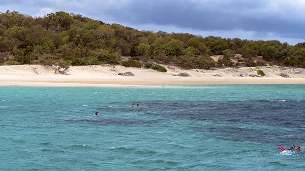 Gente haciendo snorkel en un arrecife de coral poco profundo cerca de una isla de arena — Foto de Stock