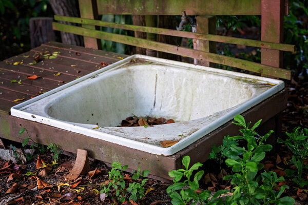 An old bathtub left abandoned and dirty in an outdoor garden, surrounded by weeds