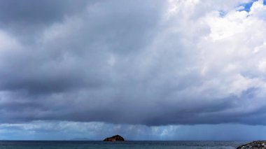 Denizde bir adanın üzerinde yağmur bulutları oluşuyor.
