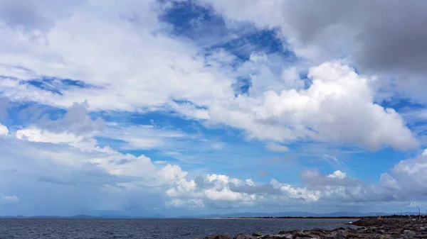 Blue cloudy sky over the ocean, with a harbour rock wall in the foreground