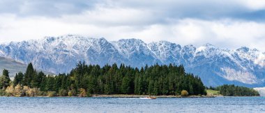 Wakatipu Gölü kıyılarında heyecan arayan bir jet motoru. Orman ve karlı dağlık arka planda.