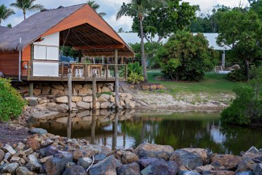 Sazlı çatısı olan ve manzaralı küçük bir göle bakan direklere asılmış açık hava yemek salonu.