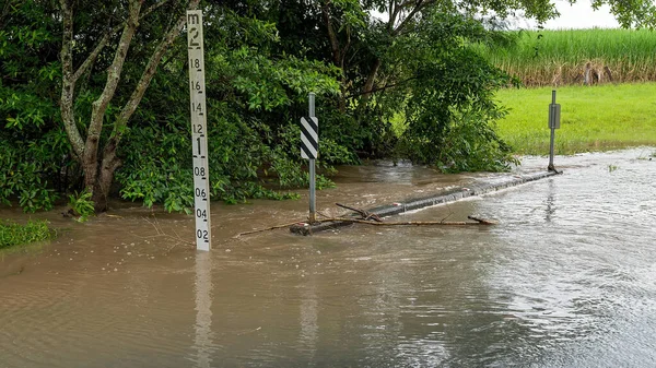 Water over the road from an overflowing creek caused by heavy tropical rainfall. Sign indicates depth.