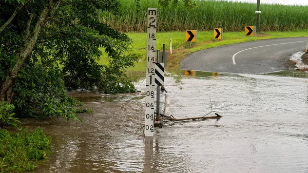 Water over the road from an overflowing creek caused by heavy tropical rainfall. Sign indicates depth.