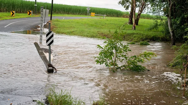 Water over the road from an overflowing creek caused by heavy tropical rainfall. Sign indicates depth.