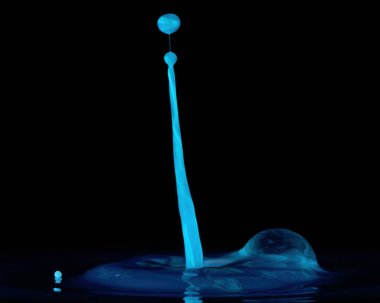 Mavi su damlaları siyah bir zemine çarpıyor.