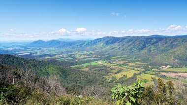 Bir dağın tepesinden, şeker kamışı tarlalarıyla benekli kırsal bir vadiye ve yol boyunca kıvrılan bir yola bakın.