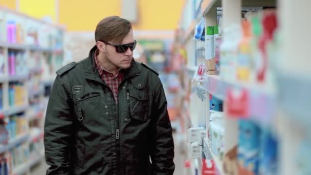 En ung man i svart jacka och solglasögon stjäl i en affär — Stockvideo