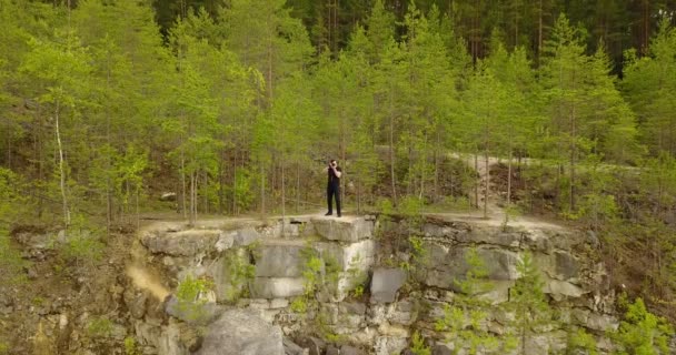 Фотограф стоит на камне и фотографирует — стоковое видео