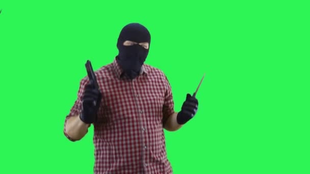 A man in a black mask and a plaid shirt in his hands holds a knife and a pistol dancing, on a green background — Stock Video