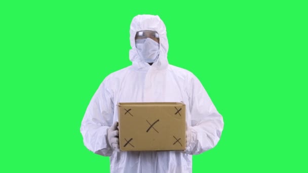 Muž v ochranném obleku a ochranné masce a brýlích drží krabici se stopováním — Stock video
