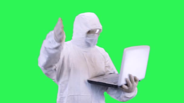 Un homme en masque et lunettes avec une combinaison de protection sur fond vert, jure avec son interlocuteur sur un ordinateur portable — Video