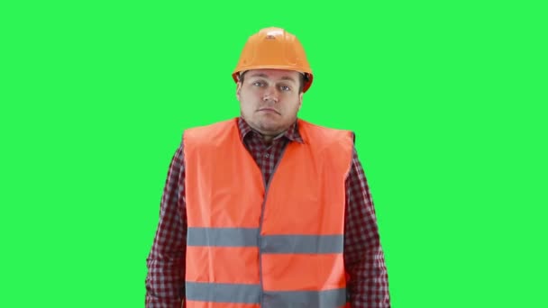 Человек в строительном шлеме и оранжевом жилете пожимает плечами, зеленый экран background.close-up — стоковое видео