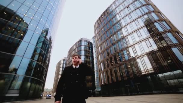 Homme d'affaires vêtu d'un manteau noir sur le fond d'un centre d'affaires parlant au téléphone — Video