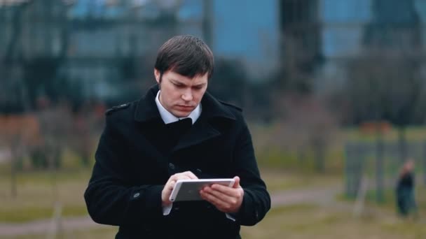 Un homme d'affaires en manteau noir regarde des informations sur une tablette — Video