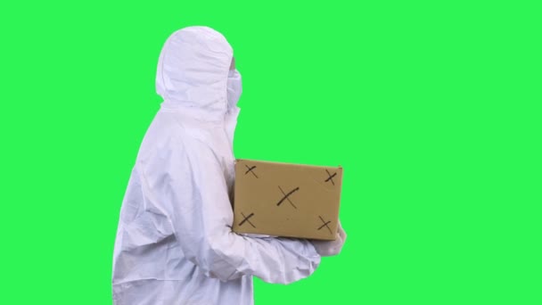 Koruyucu takım elbiseli bir adam koruyucu bir maskeyle yürür ve gözlüklü bir kutu taşır. — Stok video