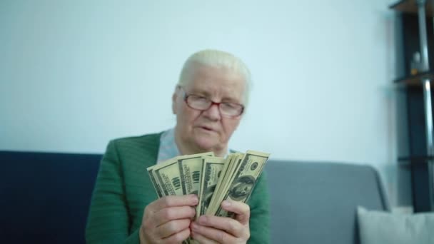 Abuela sentada en el sofá, cuenta el dinero — Vídeo de stock