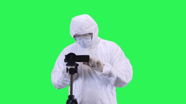 A man in a protective suit and goggles is filming a video camera with a tripod and looking at the object.Green screen background. — Stock Video