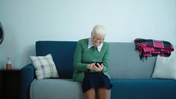 A avó está sentada no sofá a surfar ao telefone. — Vídeo de Stock