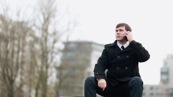 Un hombre de negocios sentado en un banco contesta el teléfono . — Vídeo de stock