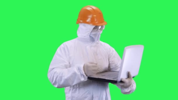 Un hombre en un casco y un traje de protección está hablando en un ordenador portátil a través de la comunicación de vídeo, gracias a su interlocutor.Fondo de pantalla verde . — Vídeo de stock