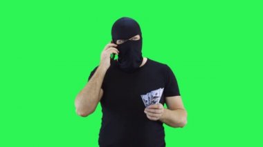 Maskeli bir adam elinde para tutarak telefonda konuşuyor. Kar maskesi. Yeşil ekran arka plan..