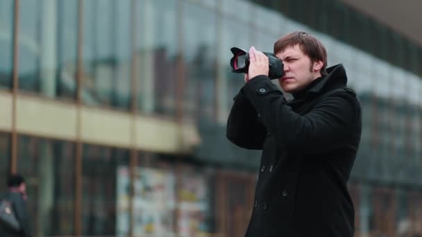 Um fotógrafo de casaco preto fica na rua fazendo uma série de quadros — Vídeo de Stock