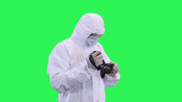 Un hombre con un traje protector y gafas selecciona cuidadosamente el modo de disparo en la videocámara. Fondo de pantalla verde . — Vídeo de stock