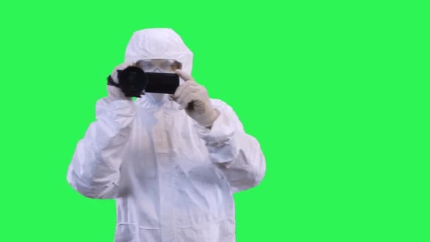 Um homem em um terno de proteção e óculos está filmando uma câmera de vídeo com suas mãos.Fundo de tela verde . — Vídeo de Stock