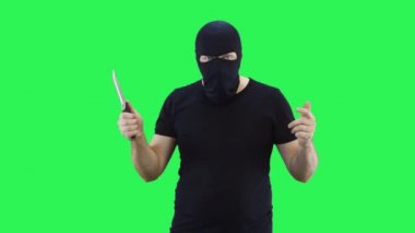 Siyah maskeli bir adam elinde bir bıçak tutuyor ve düşmanın kötü hissedeceğini gösteriyor. Kar maskesi. Yeşil ekran arka plan..
