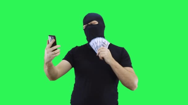 Seorang pria bertopeng berbicara melalui video panggilan memegang uang di hand.Balaclava.Green latar belakang layar. — Stok Video