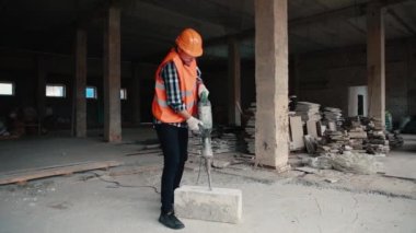 Turuncu yelek ve turuncu kasklı bir müteahhit matkapla çalışıyor..