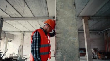 Turuncu yelekli ve turuncu kasklı bir adam kafasını bir sütuna çarpıyor..