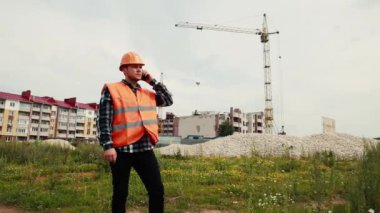 Miğferli bir müteahhit inşaat halindeki bir evin arka planındaki telefon verileriyle konuşur..