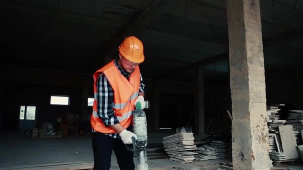 Un uomo con un giubbotto arancione e un casco arancione sta lavorando con un martello pneumatico . — Video Stock