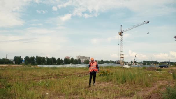 Un constructor con chaleco naranja y casco naranja camina en el walkie-talkie . — Vídeos de Stock