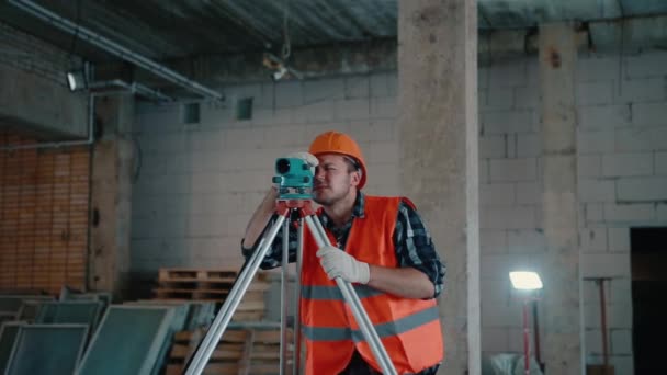 Un homme vêtu d'un gilet orange et d'un casque orange regarde dans un appareil de mesure . — Video