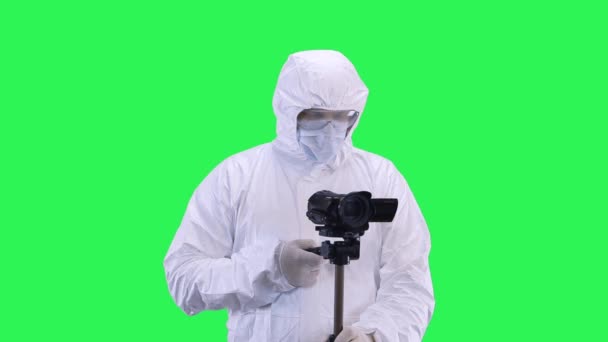 A man in a protective suit and goggles is filming a video camera with a tripod.Green screen background. — Stock Video