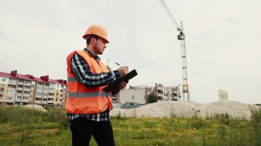 Miğferli bir müteahhit inşaat halindeki bir evin arka planına karşı veri yazar..