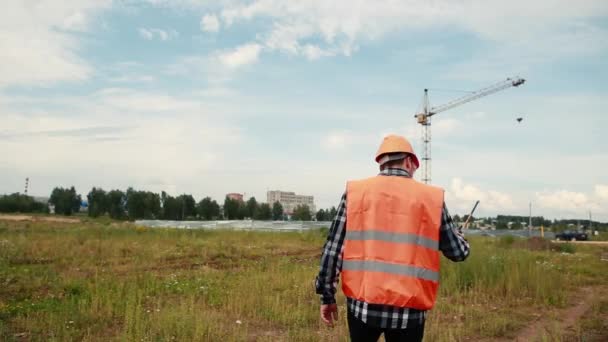 El constructor en un chaleco naranja va a la grúa dando instrucciones sobre el walkie-talkie . — Vídeo de stock