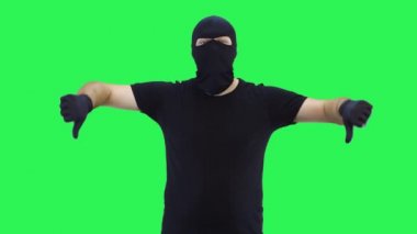 Kar maskeli bir adam iki parmak aşağıda, yeşil ekran bir arka plan gösteriyor.