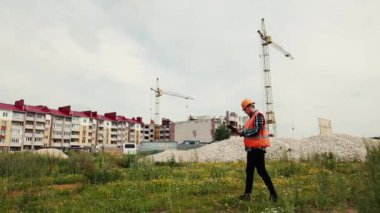 Miğferli ve yelekli bir müteahhit, inşaat halindeki bir evin arka planındaki veri klasöründeki verilere bakıyor..